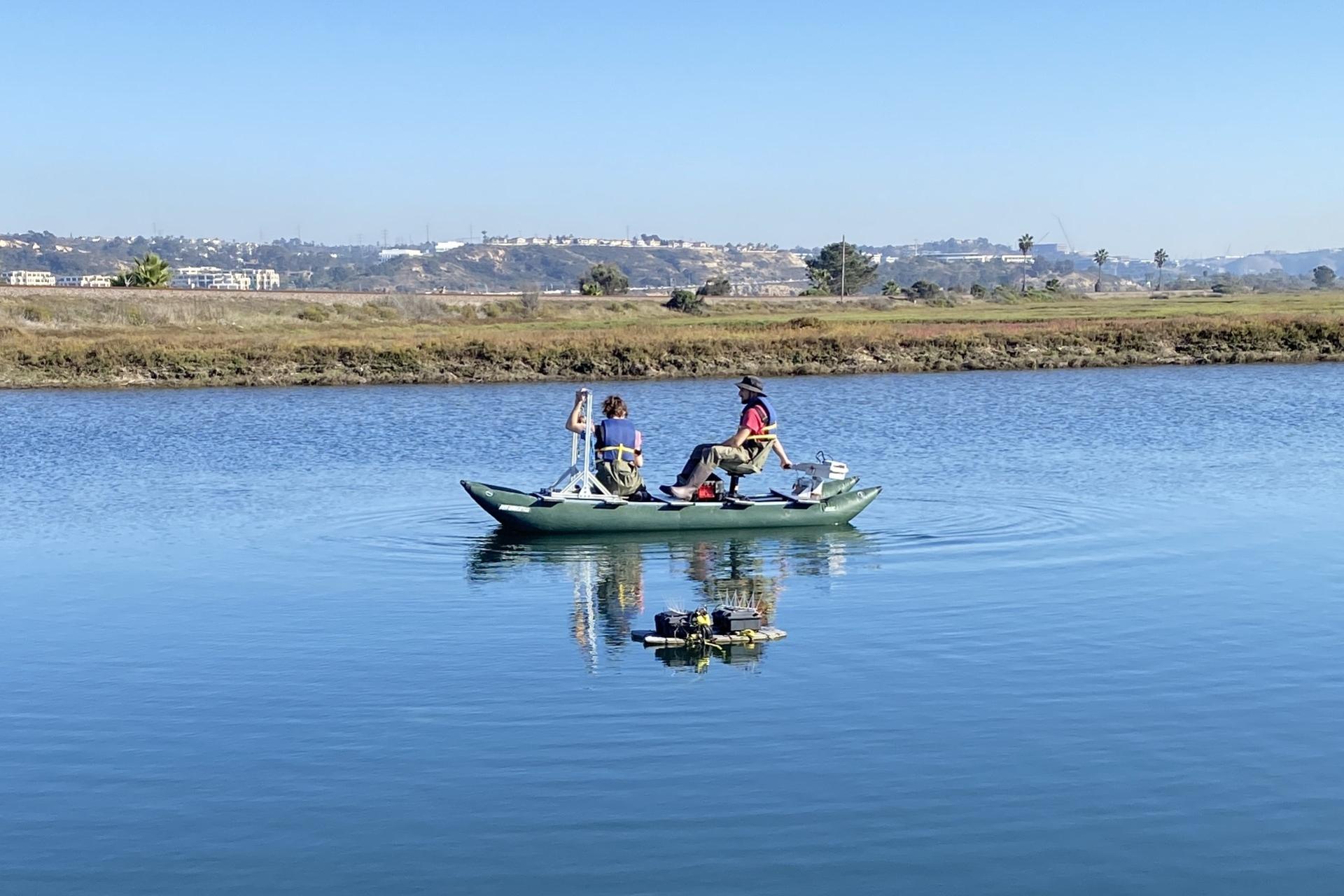 Two people on a boat deploying equipment in the water.