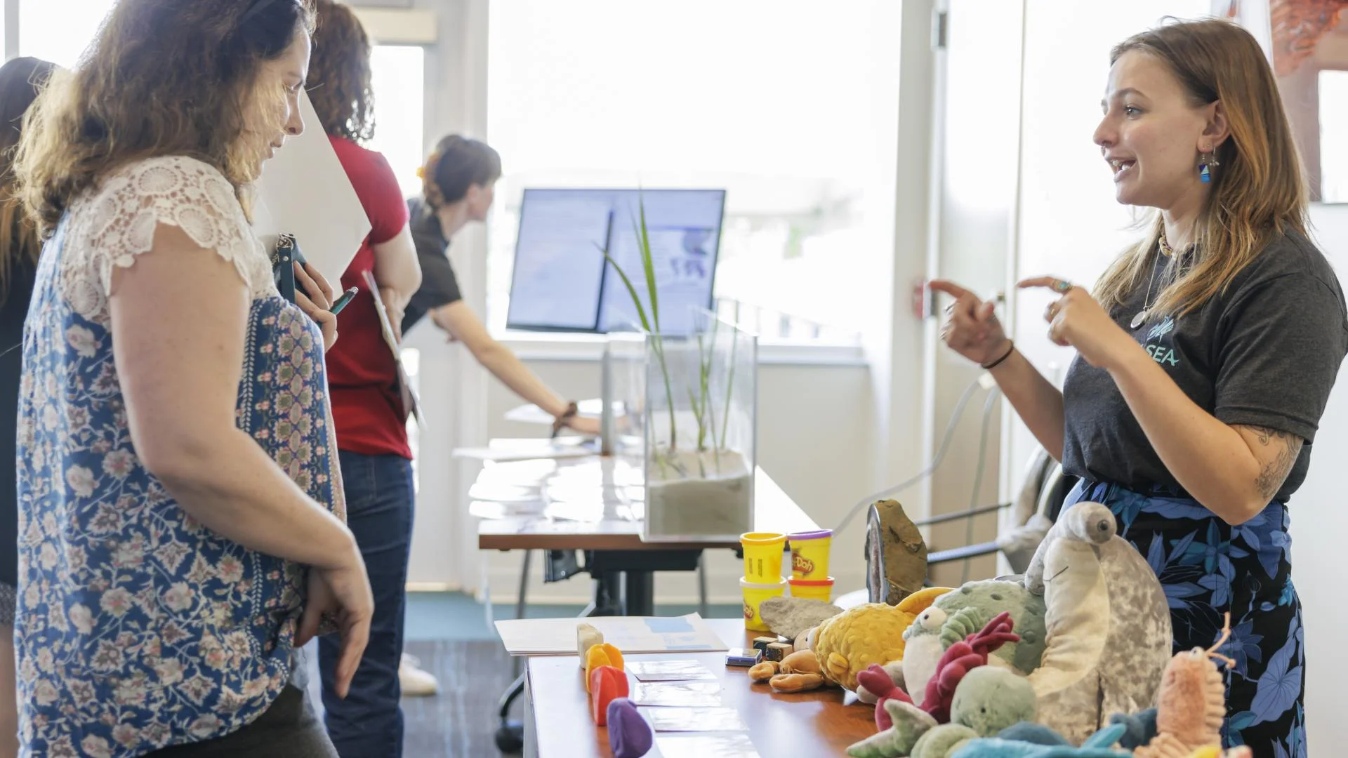 Person on the right is showing off various sea life plushies to a person on the left