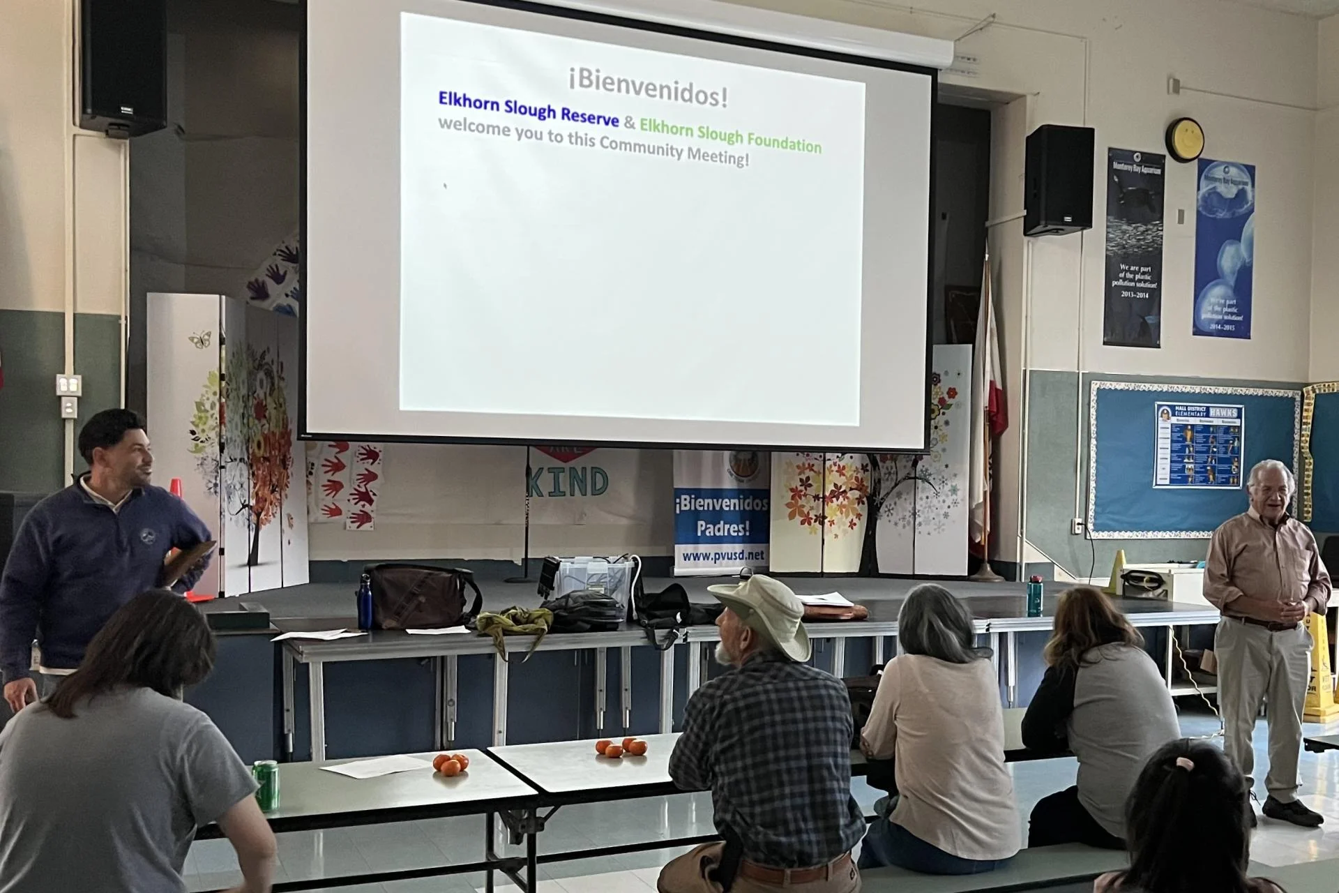Two people are presenting slides shown on the projector screen.