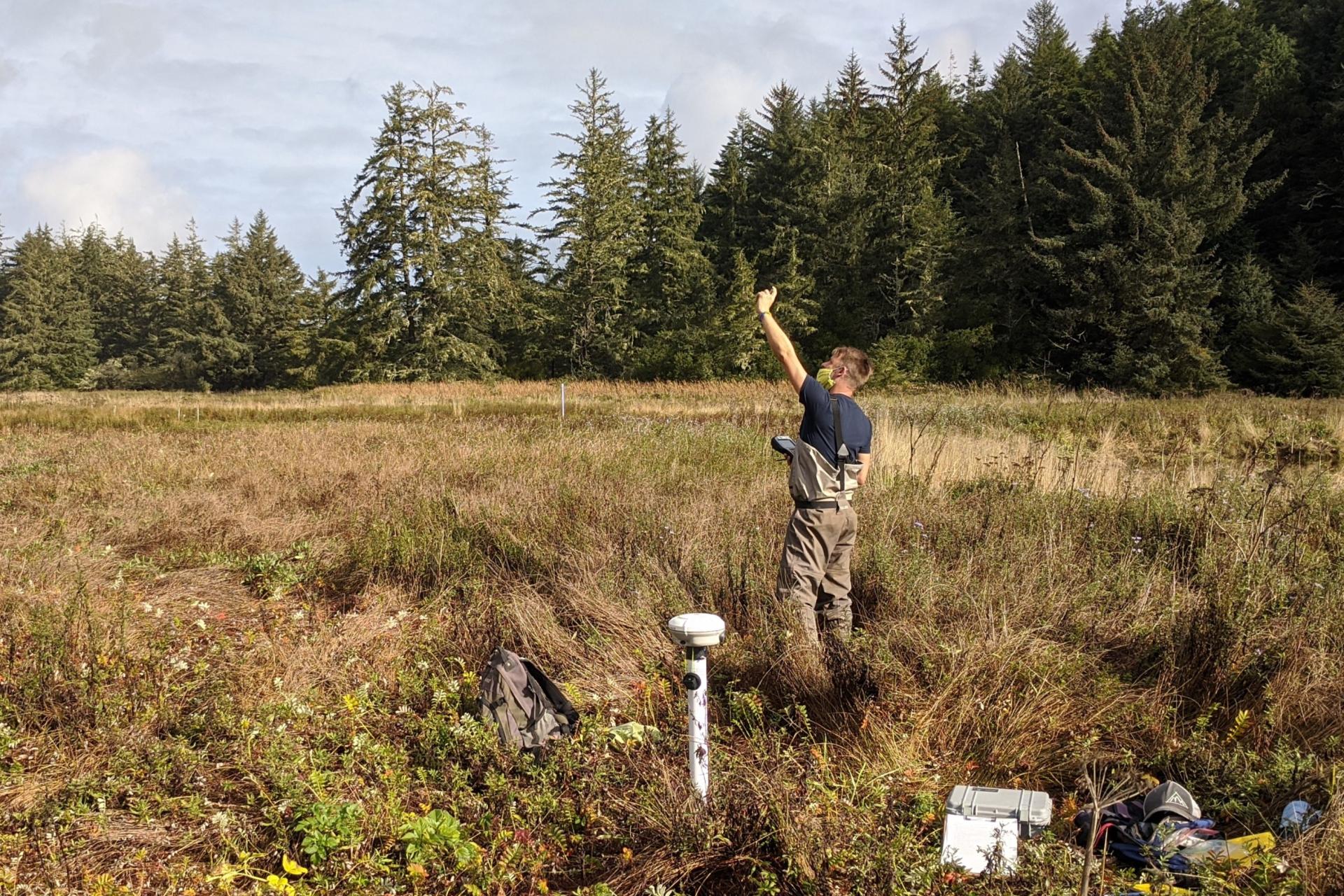 Person standing in a field point next to an instrument and pointing at the sky.