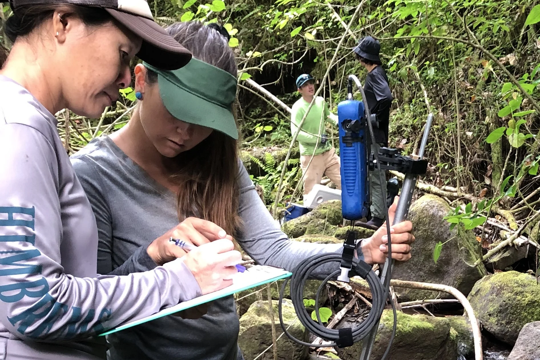 Two people standing. One person is writing on a clip board while the other person is holding a water-related instrument.