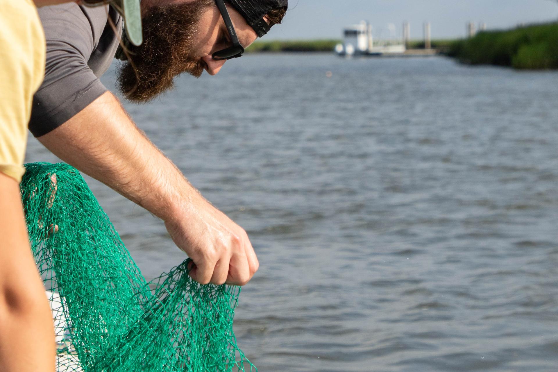 Individual bending over edge of boat and pulling up net