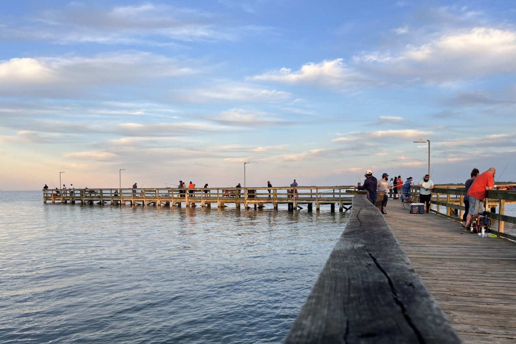 People standing on a pier. Some are fishing over the edge.