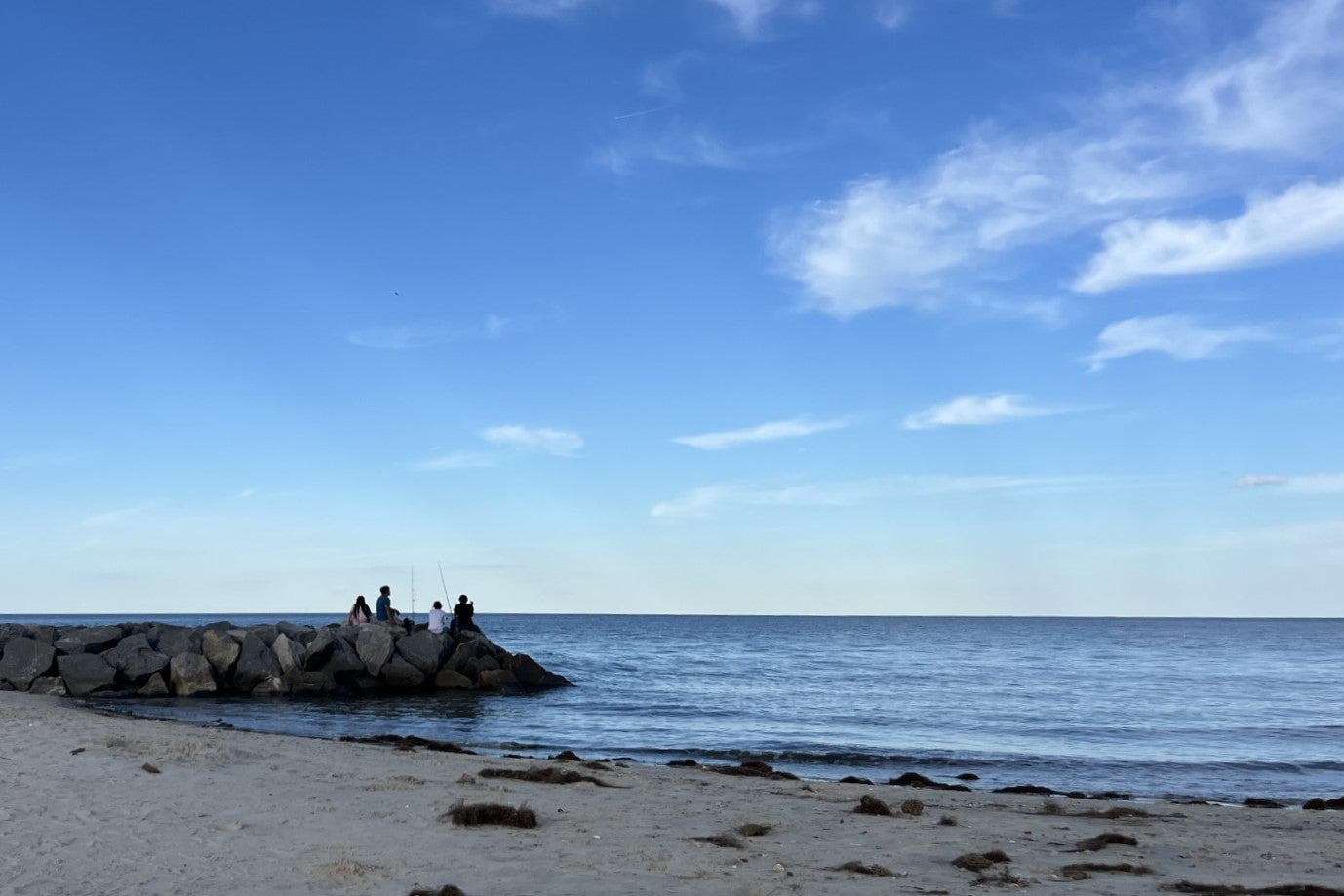 Group of people sitting on rock pile that extends into the ocean